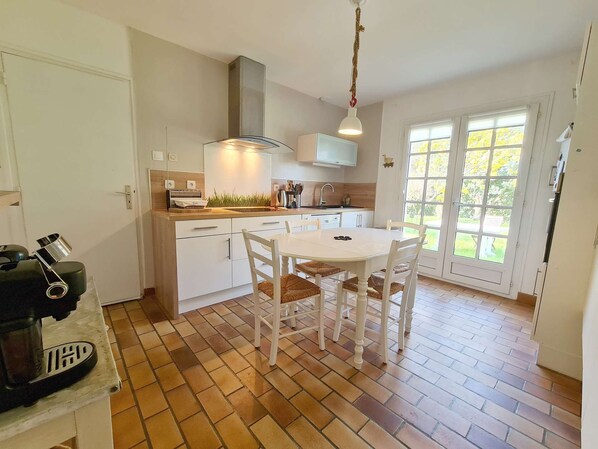 A kitchen with a dining table, chairs, a hanging light fixture, and a window with a view of greenery.