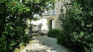 A gravel pathway leading to a stone building with a boat docked outside. - Maison 2 Chambres Proche Commerces à Louer Pour les Vacances (ARZON)