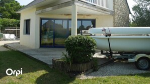 A house with a covered porch, a water tank on a trailer, and a small garden. - Maison 2 Chambres Proche Commerces à Louer Pour les Vacances (ARZON)