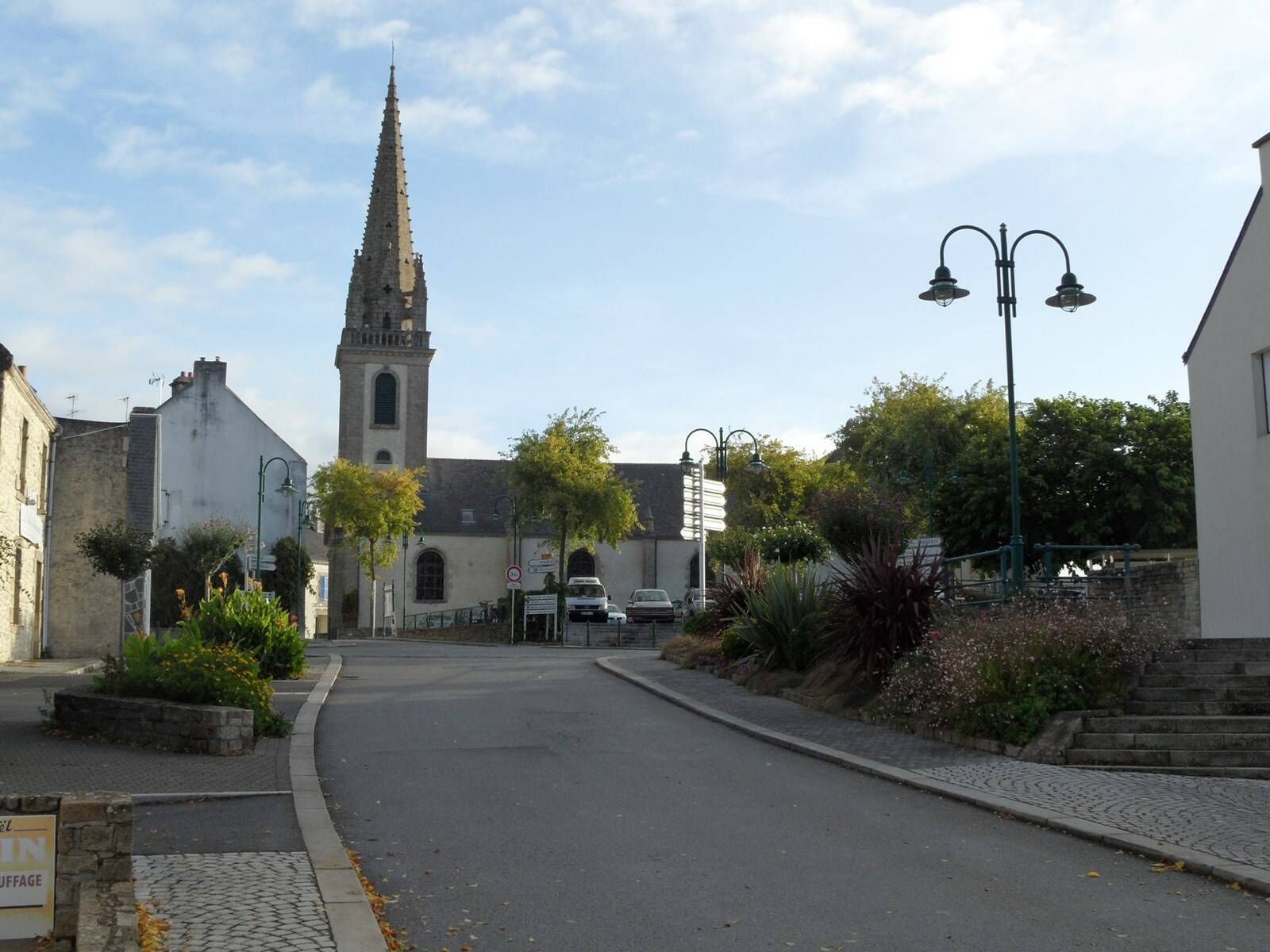 A street leading to a church with a tall spire, surrounded by buildings and greenery.