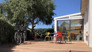 Une terrasse en bois avec un vélo, des sièges d’extérieur et un bâtiment doté de grandes fenêtres.