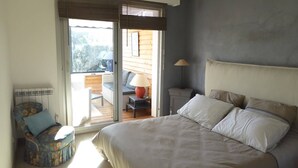 Une chambre avec un grand lit, une table de chevet, une lampe, une chaise et une vue sur l’extérieur grâce à une porte coulissante.