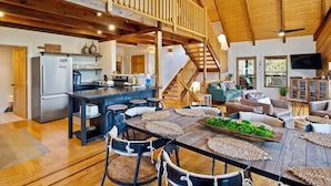 Un vaste espace de vie doté d’un plafond en bois, une cuisine équipée d’un réfrigérateur et une table à manger avec des chaises.