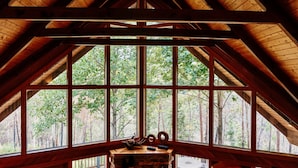 Une cabane dotée d’un grand espace mezzanine avec de larges fenêtres, d’une cheminée et d’une terrasse visible de l’extérieur.