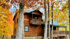 Une cabane en bois dotée d’un balcon, entourée d’arbres aux feuilles d’automne.