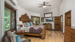 A bedroom with a wooden bed, a ceiling fan, a large window, and a wooden dresser.