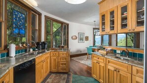 A kitchen with wooden cabinets, a dishwasher, and a window with a view of trees.