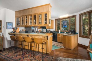 Une cuisine dotée de meubles en bois, d’un coin bar avec des tabourets et d’une grande fenêtre laissant entrer la lumière naturelle.