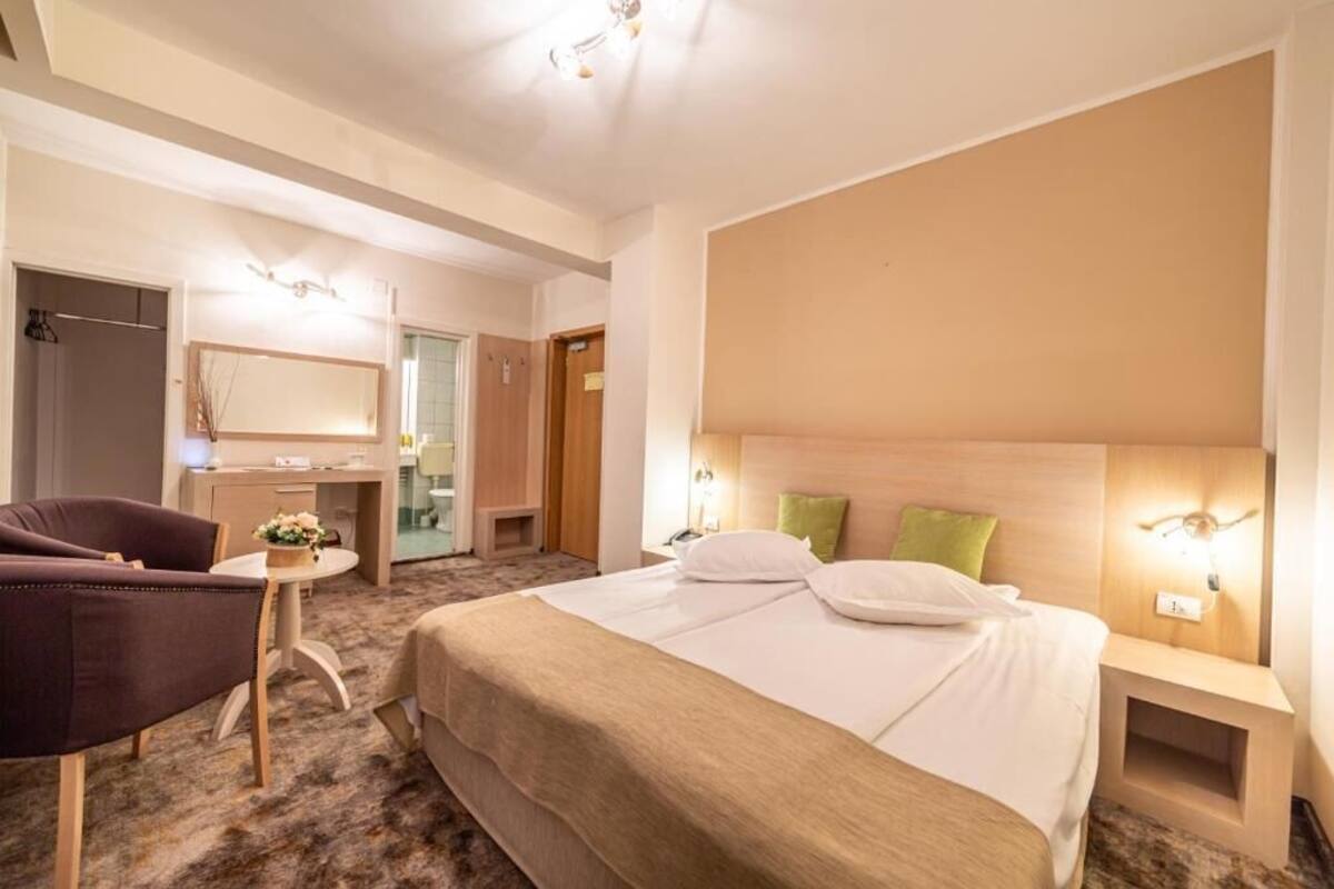 A hotel room with a large bed, a desk with a chair, a mirror, and a small table with a vase.