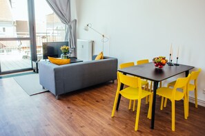 A modern living room with a grey sofa, yellow chairs, a dining table with fruit and candles, and a large window with a view of buildings. - Fantastic Loft with Balcony (Berlin)
