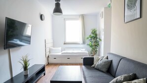 Ein modernes Wohnzimmer mit Flachbildfernseher, grauem Sofa, Couchtisch und einer kleinen Pflanze.