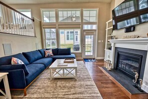A living room with a sectional sofa, a fireplace, a television, and large windows. - Coastal Club * 5 BR w 2.5 Bath Beach House (Lewes)