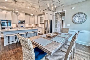 A modern kitchen with stainless steel appliances, a dining area with a wooden table, and a large wall clock. - Coastal Club * 5 BR w 2.5 Bath Beach House (Lewes)