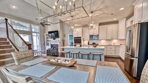 A modern kitchen with a central island, bar stools, and a dining area with striped placemats.