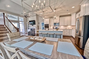 A modern kitchen with a central island, bar stools, and a dining area with striped placemats.