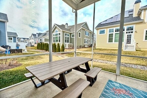 A covered patio with a picnic table and benches, overlooking a residential area with houses.