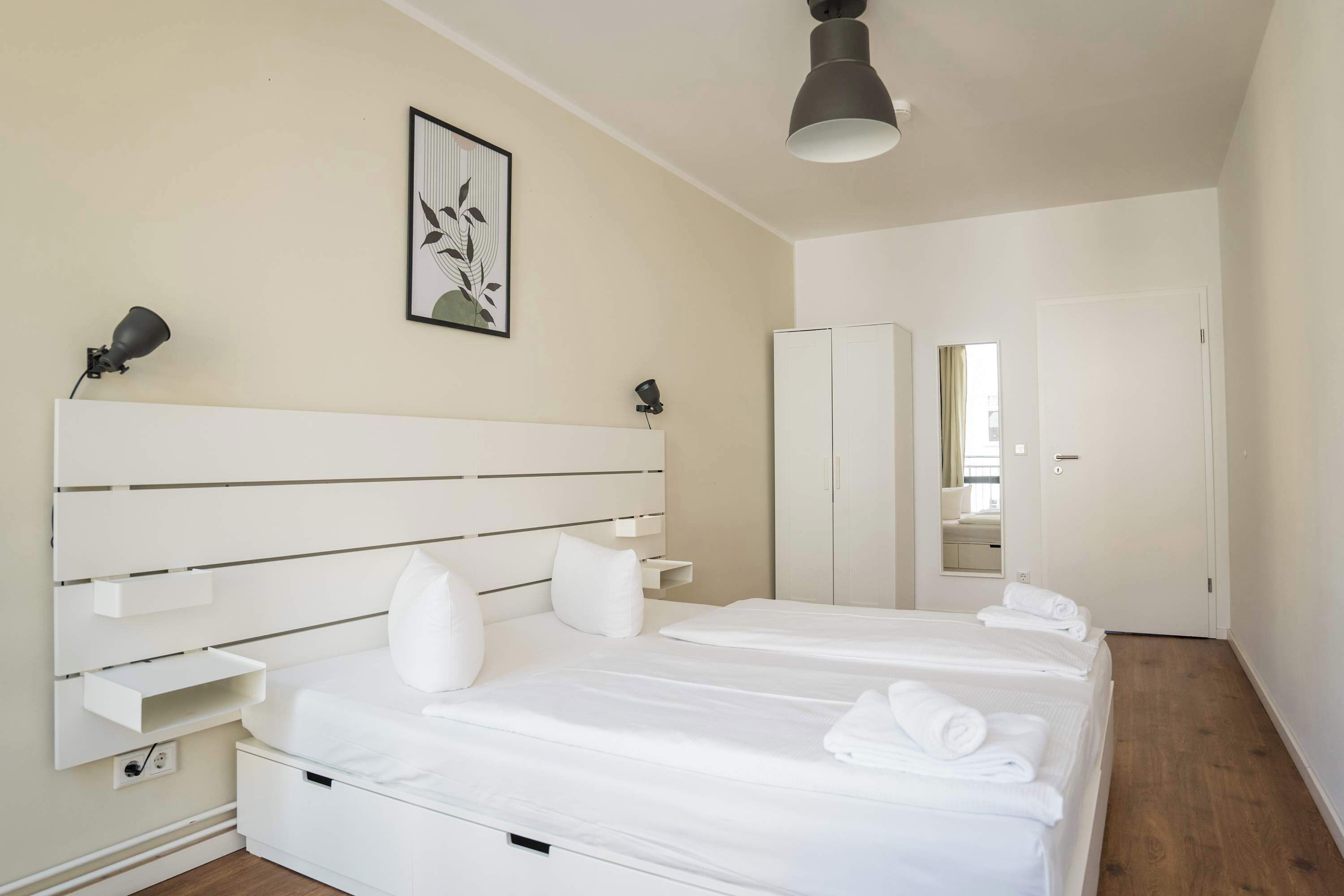 Ein modernes Hotelzimmer mit einem großen Bett, Nachttischen, einem Kleiderschrank und einem Spiegel.