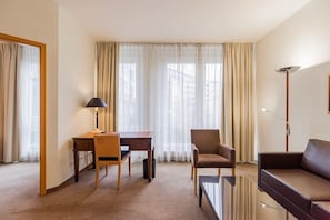 A hotel room with a desk, chair, sofa, and a floor lamp.