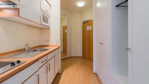 A compact kitchen with a microwave, sink, and wooden countertop. A hallway leads to a closet with a door. - Deluxe Studio in Berlin Mitte (Berlin)