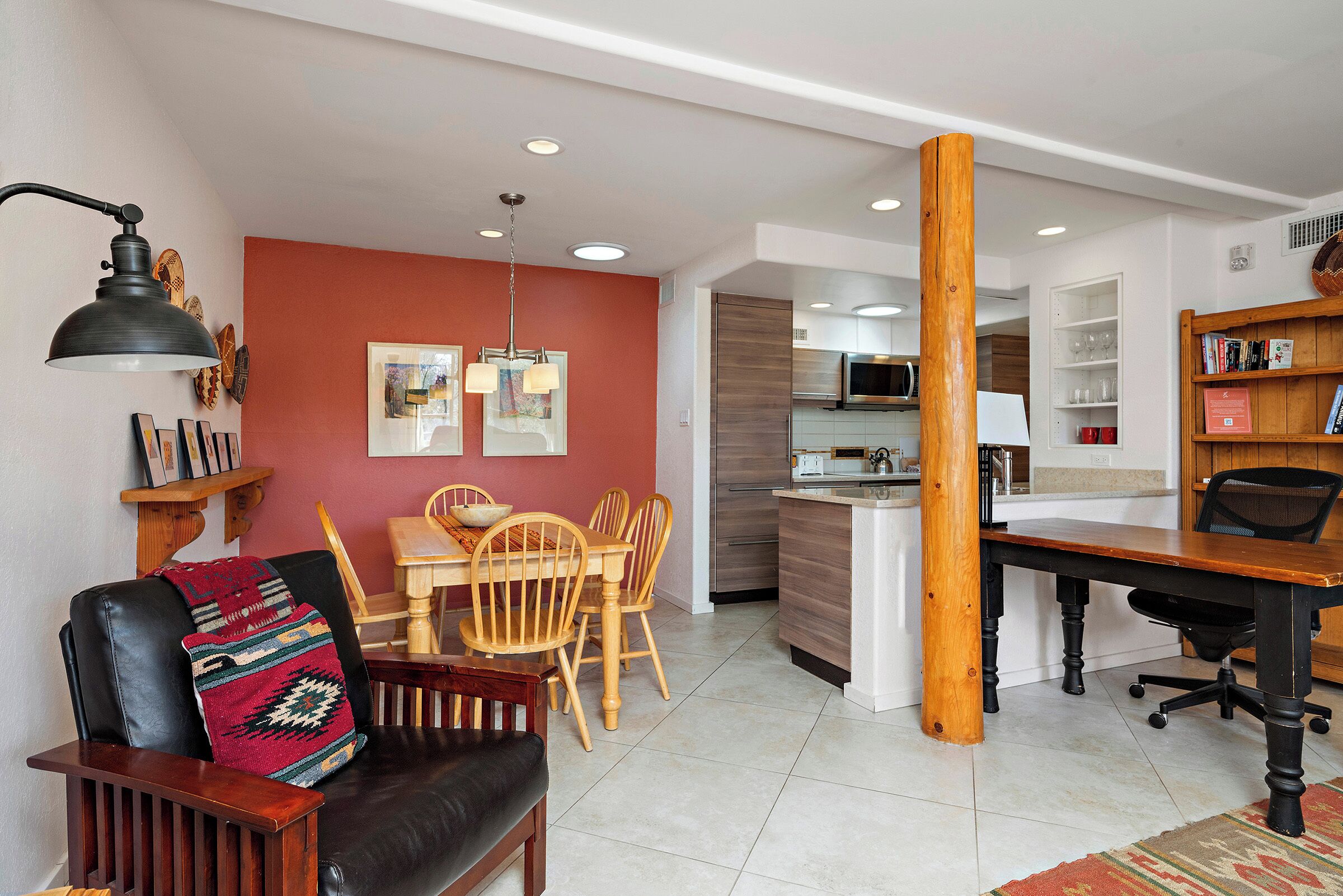 A modern living room with a dining area, kitchen, and a large wooden column.