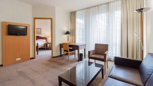 Ein Hotelzimmer mit Bett, Schreibtisch, Stuhl, Sofa, Fernseher und einem großen Fenster mit Vorhängen.