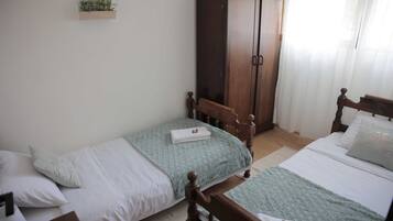 Ein Schlafzimmer mit zwei Einzelbetten, einem Holzschrank und einem kleinen Regal mit einer Pflanze.