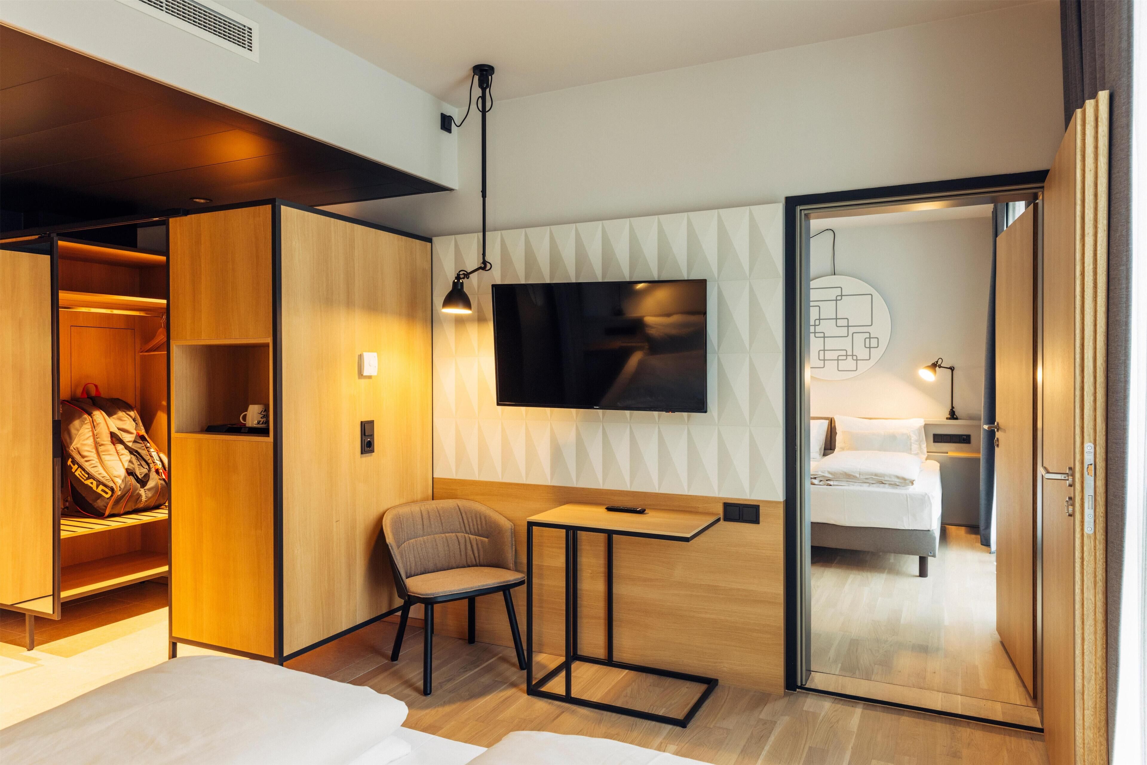 Habitación de hotel moderna con cama, escritorio, silla, armario y televisor.
