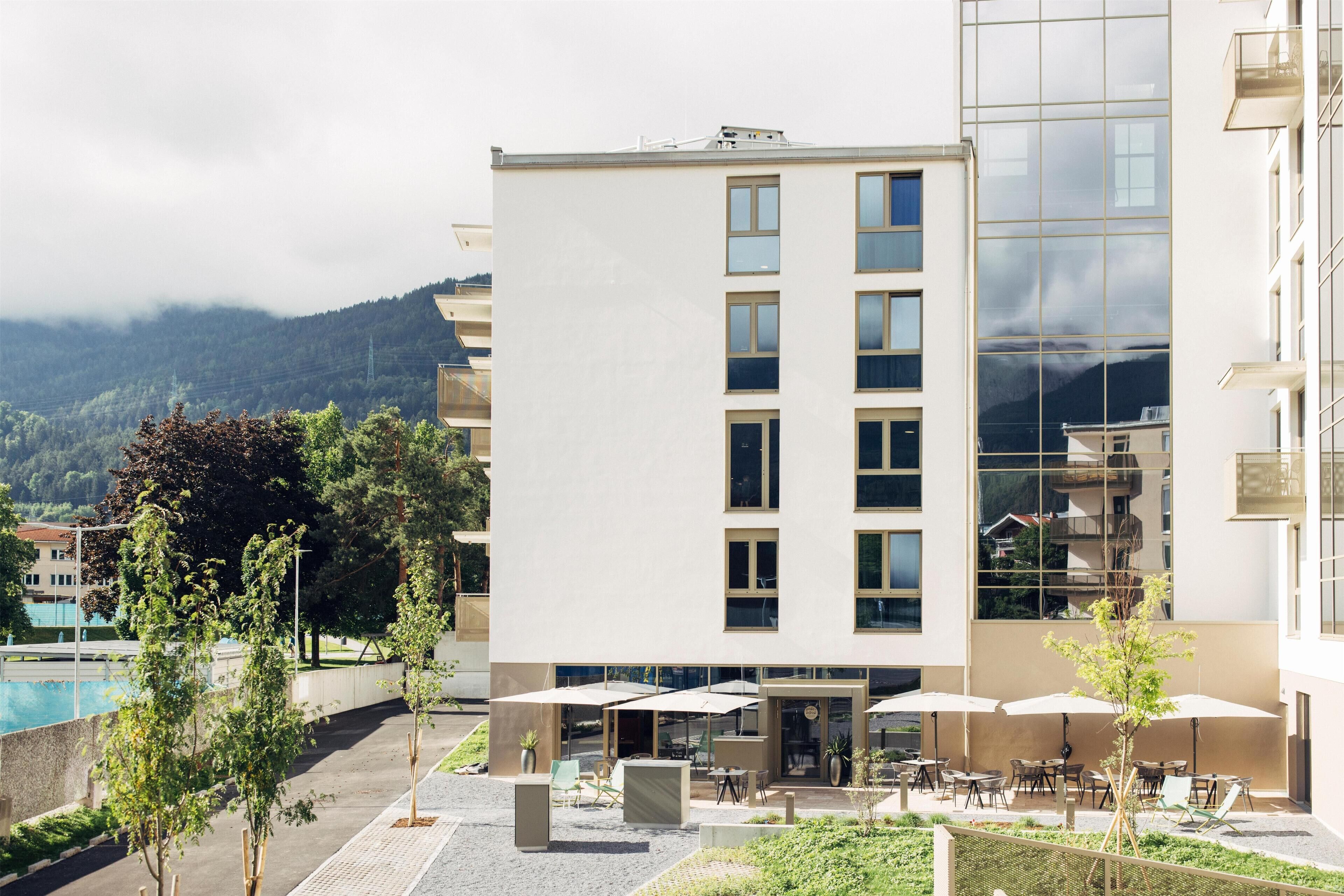 A modern building with a pool, outdoor seating, and a mountain backdrop.