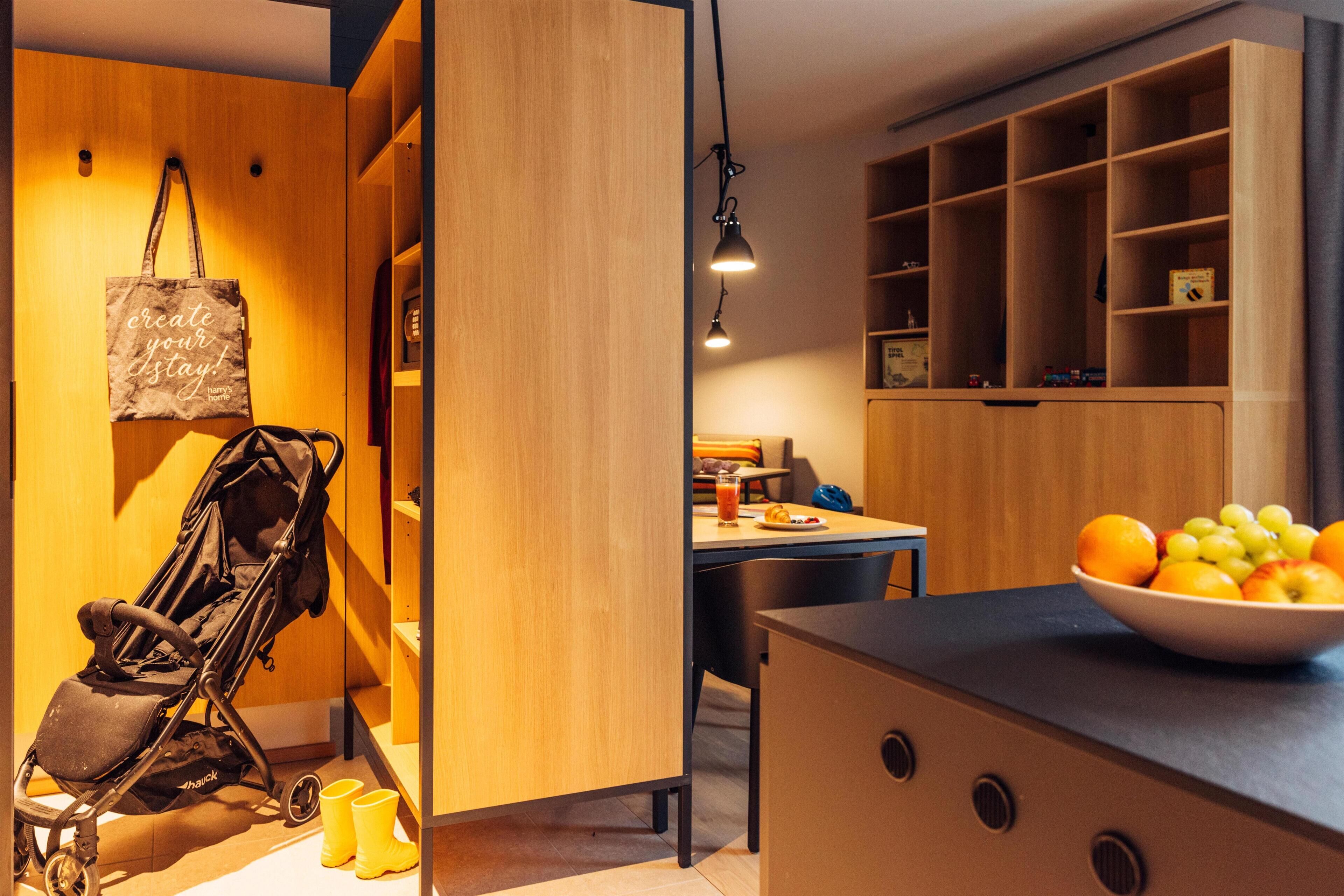 A modern kitchen with a wooden cabinet, a bowl of fruit on the counter, and a stroller with yellow shoes beside it.