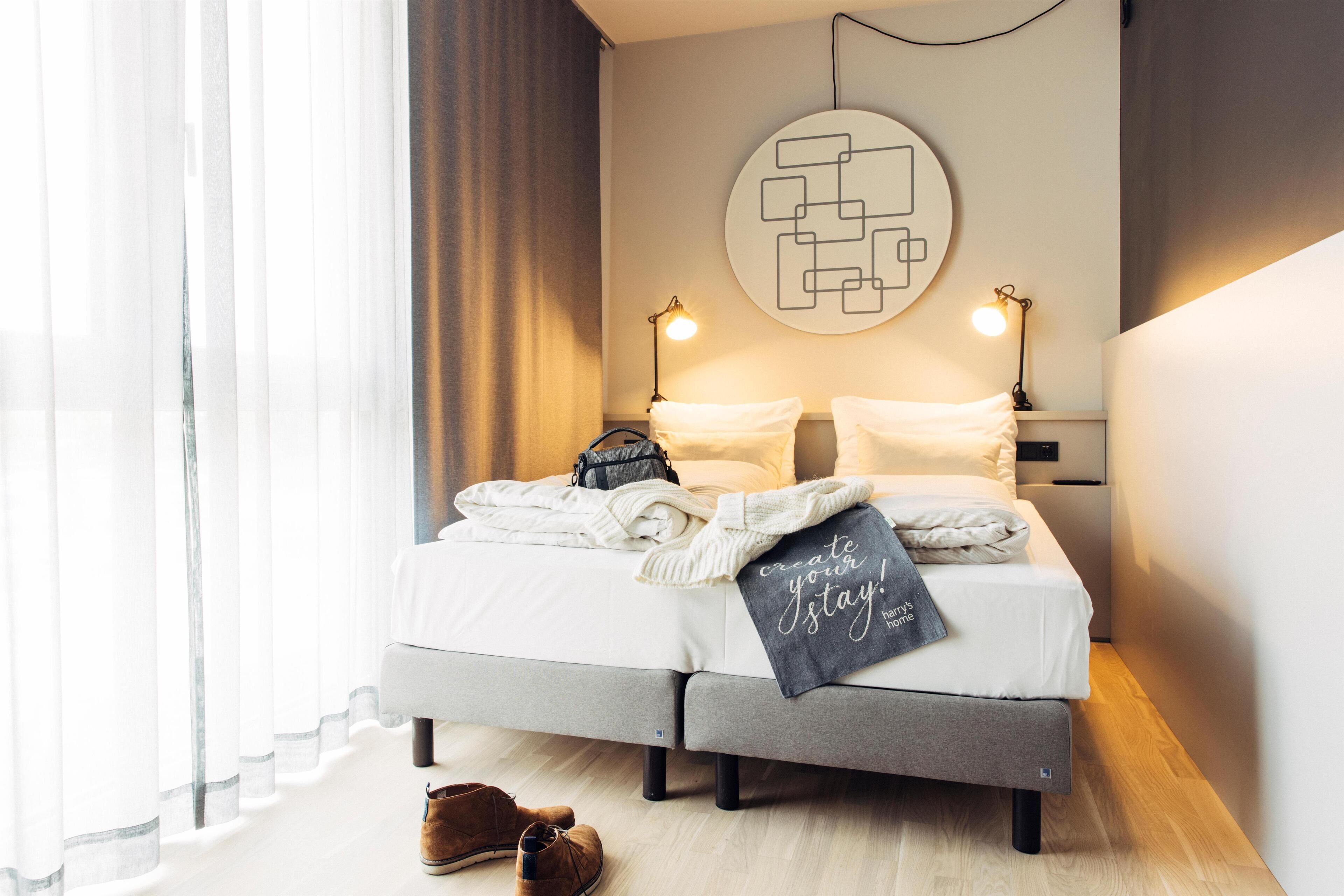 Una habitación de hotel moderna con cama, lámparas de noche, una obra de arte en la pared y una ventana con cortinas.