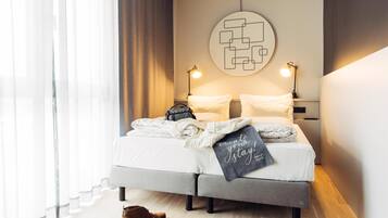 Una habitación de hotel moderna con cama, lámparas de noche, una obra de arte en la pared y una ventana con cortinas.