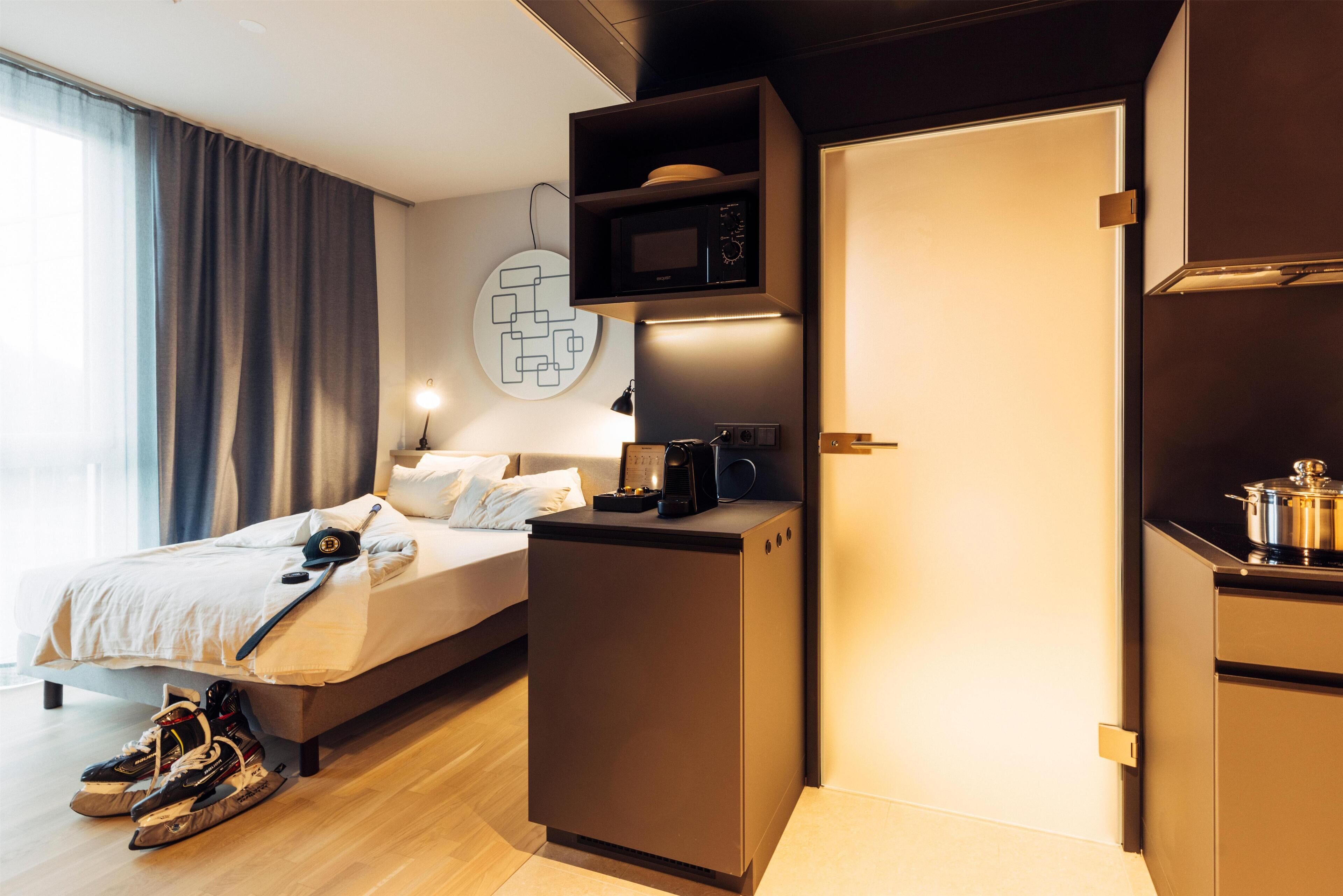 Una habitación de hotel moderna con una cama, una kitchenette pequeña y un microondas.