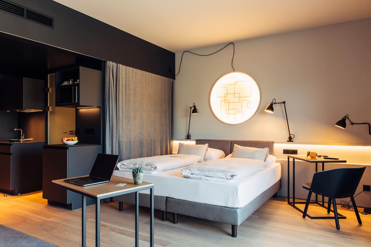 Ein modernes Hotelzimmer mit Bett, Schreibtisch, Stuhl und einer Küchenzeile.