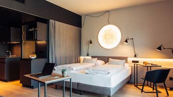 A modern hotel room with a bed, desk, chair, and kitchenette.