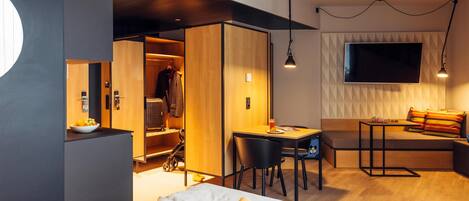 Ein modernes Hotelzimmer mit Bett, Schreibtisch, Stuhl, Fernseher und Kleiderschrank.