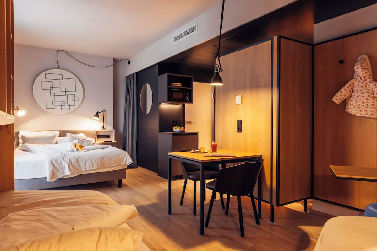Ein modernes Schlafzimmer mit Bett, Nachttisch, Lampe und einer kleinen Essecke mit Tisch und Stühlen.
