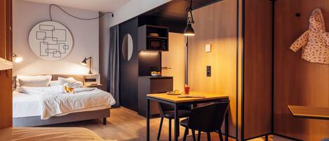 A modern bedroom with a bed, bedside table, lamp, and a small dining area with a table and chairs.