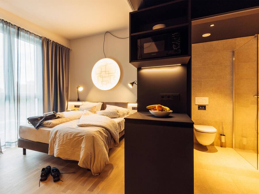A modern hotel room with a bed, bedside table, and a shower area.