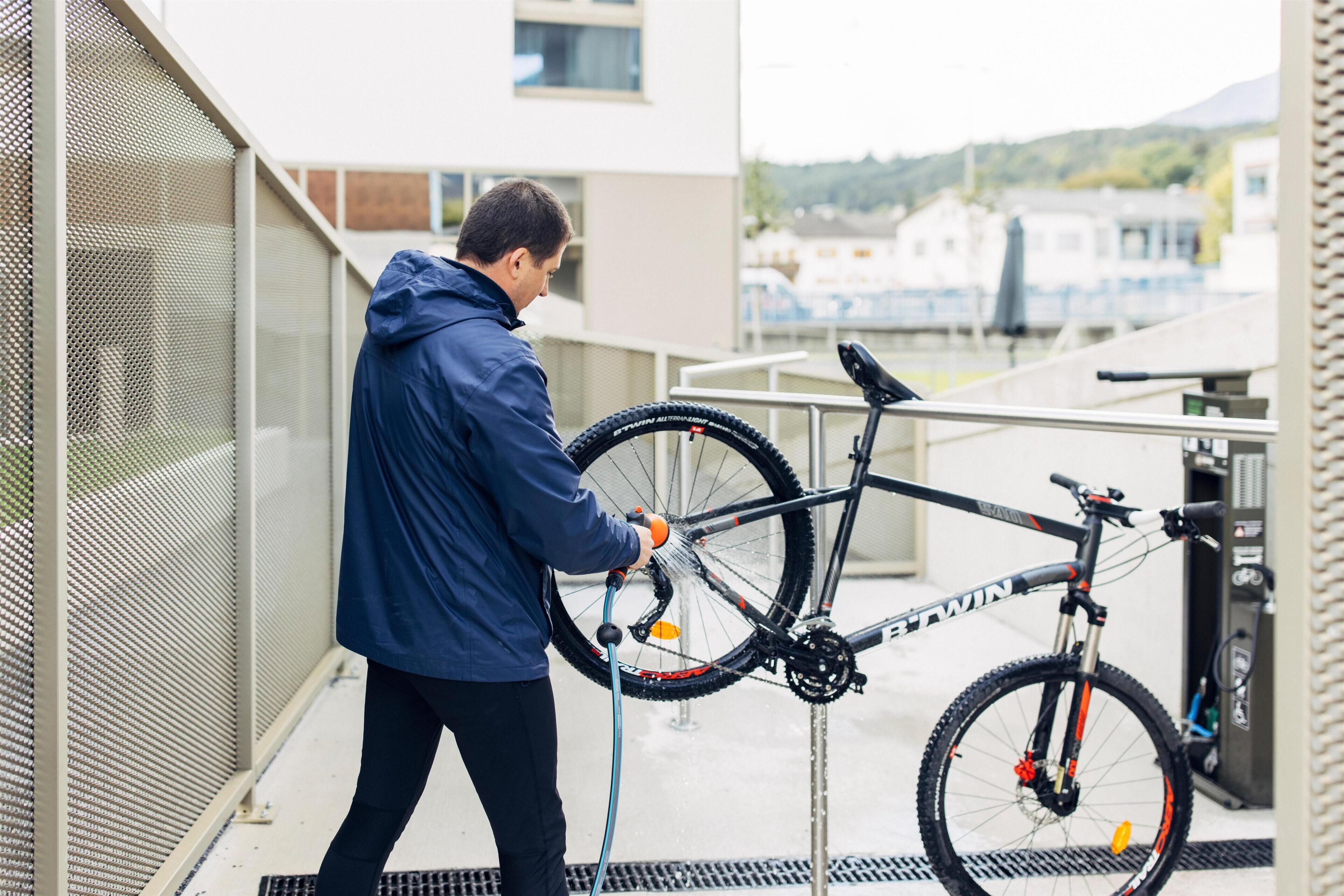 A person washing a bicycle on a balcony with a view of buildings and hills in the background.