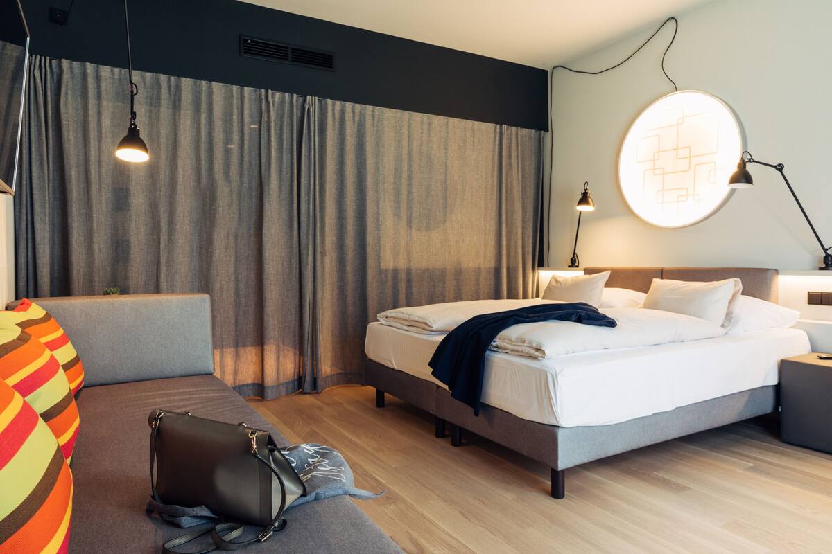 Ein modernes Hotelzimmer mit Bett, Nachttischen, Schreibtisch, Stuhl und einer Couch.