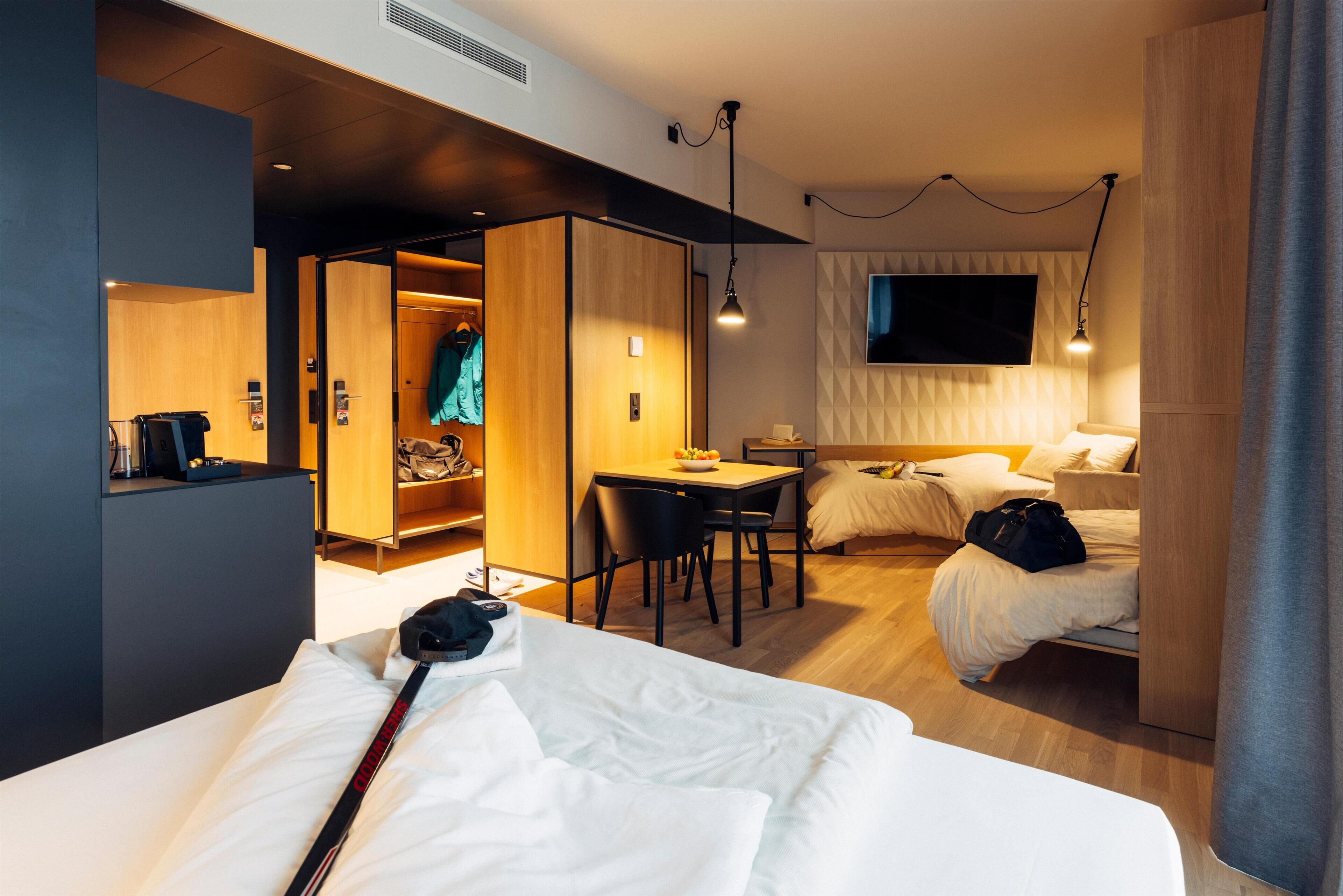 A modern hotel room with a bed, a desk, a chair, a TV, and a wardrobe.