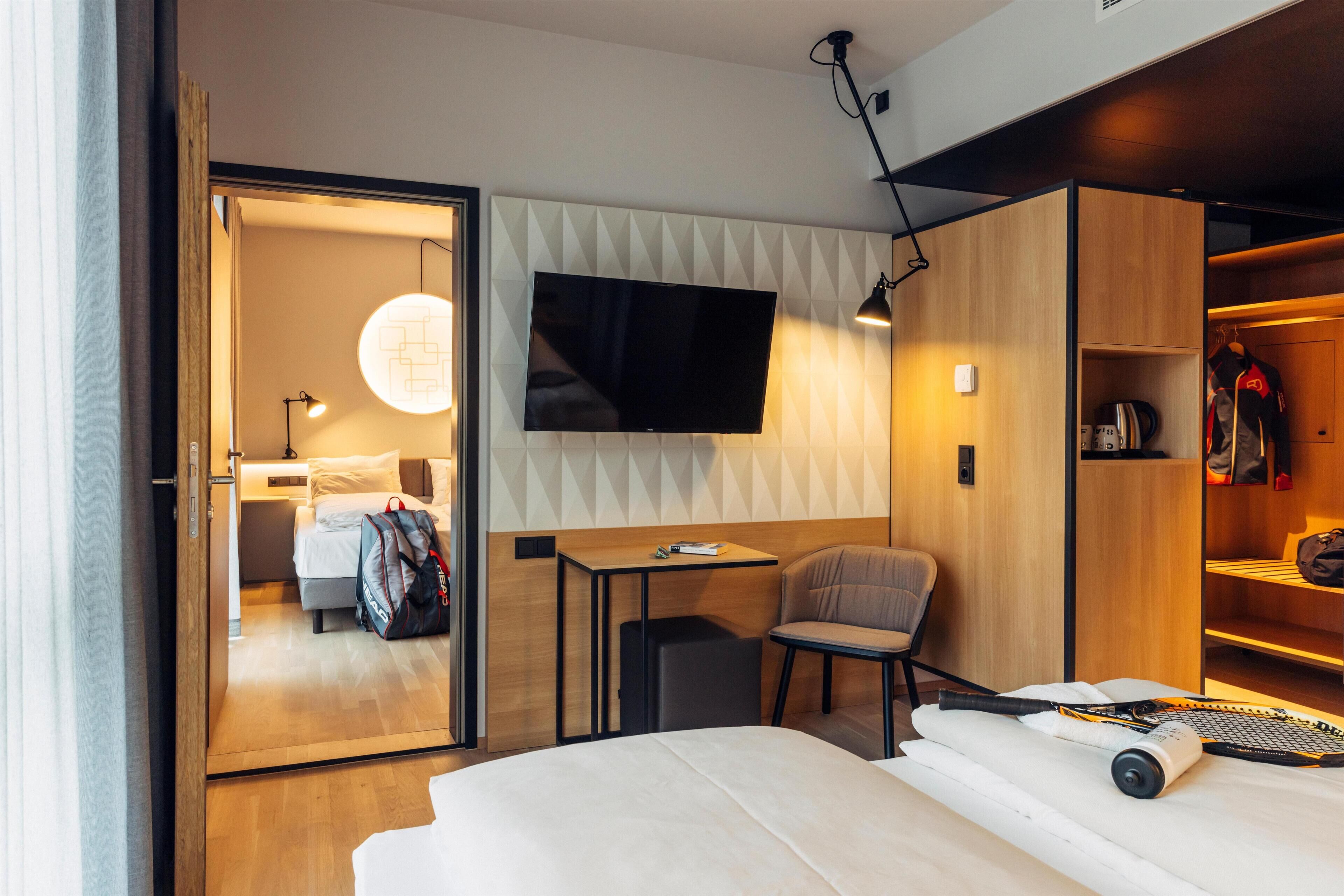 Una habitación de hotel moderna con una cama, un escritorio, una silla, un televisor montado en la pared y un armario.