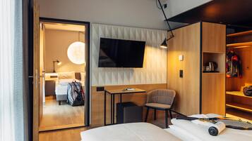 Una habitación de hotel moderna con una cama, un escritorio, una silla, un televisor montado en la pared y un armario.