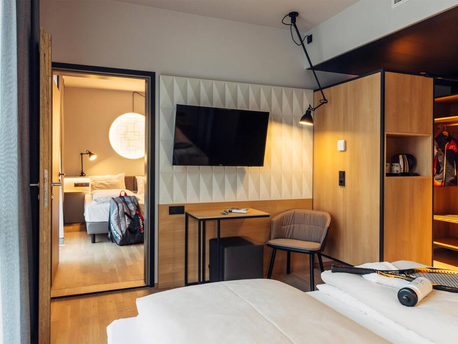 Una habitación de hotel moderna con una cama, un escritorio, una silla, un televisor montado en la pared y un armario.