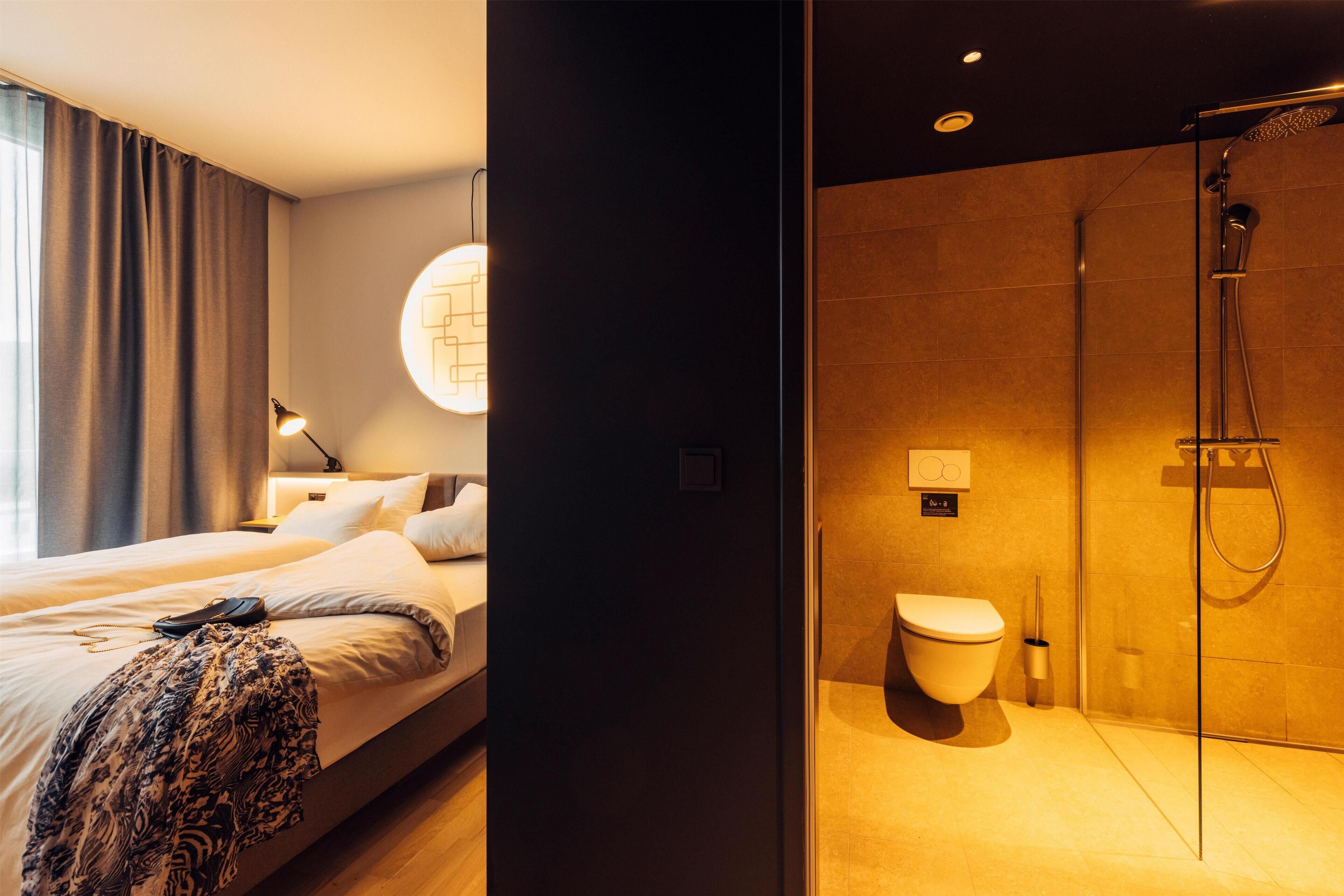 A modern hotel room with a bed, bedside table, and a large window with curtains.