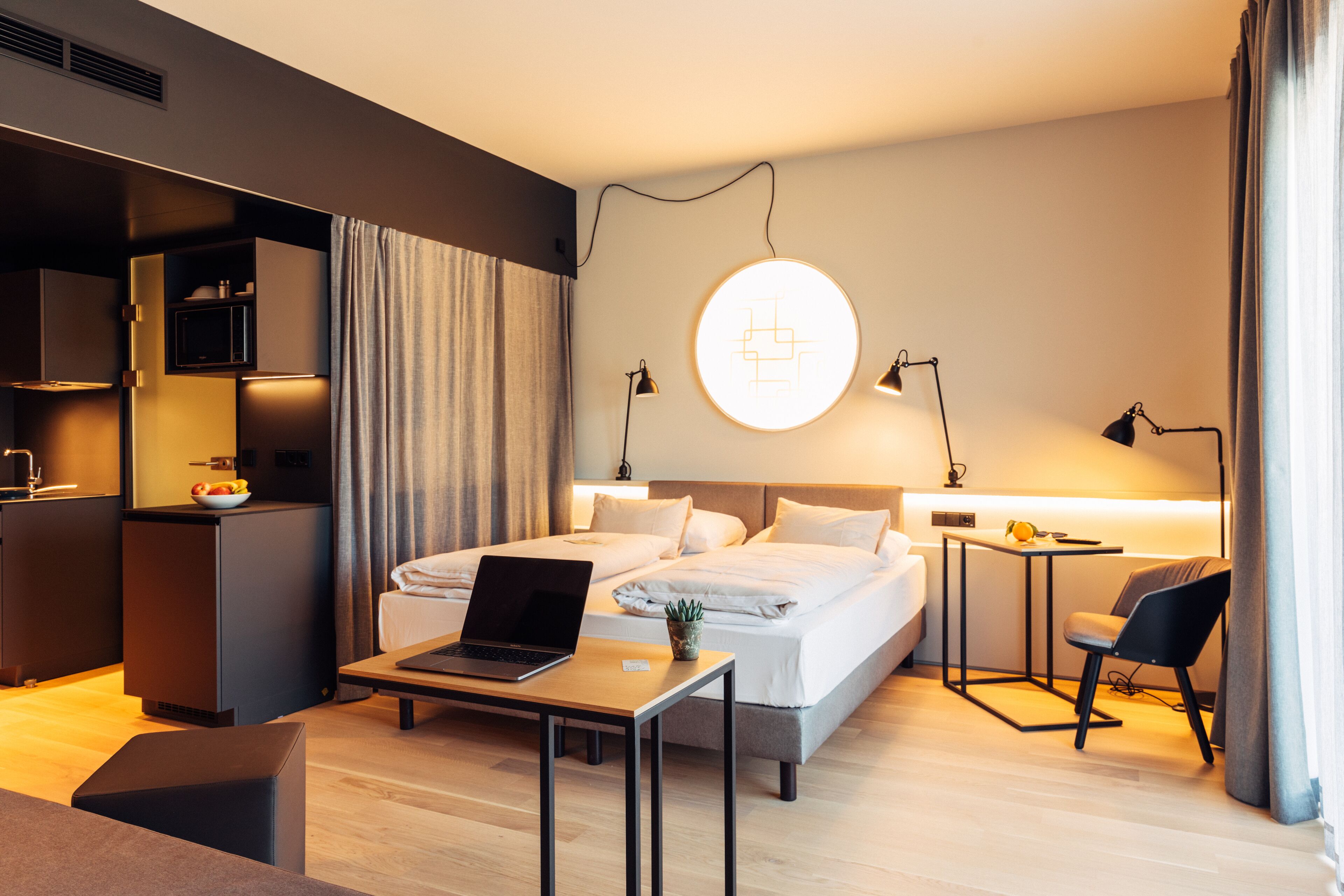 Ein modernes Hotelzimmer mit Bett, Schreibtisch, Laptop und einem kleinen Tisch mit Pflanze.
