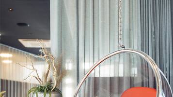 A modern interior with a hanging chair, a tall vase with plants, and a patterned floor.