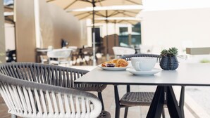 En udendørs café med fletstole, et bord med croissant, kop og en lille plante.