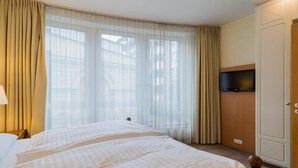 A hotel room with two beds, a television on a wooden cabinet, and large windows with curtains. - Superior Apartment in Berlin Mitte (Berlin)