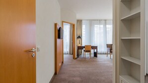Une chambre d’hôtel avec une porte en bois, un bureau avec une chaise, une télévision et une grande fenêtre avec des rideaux.